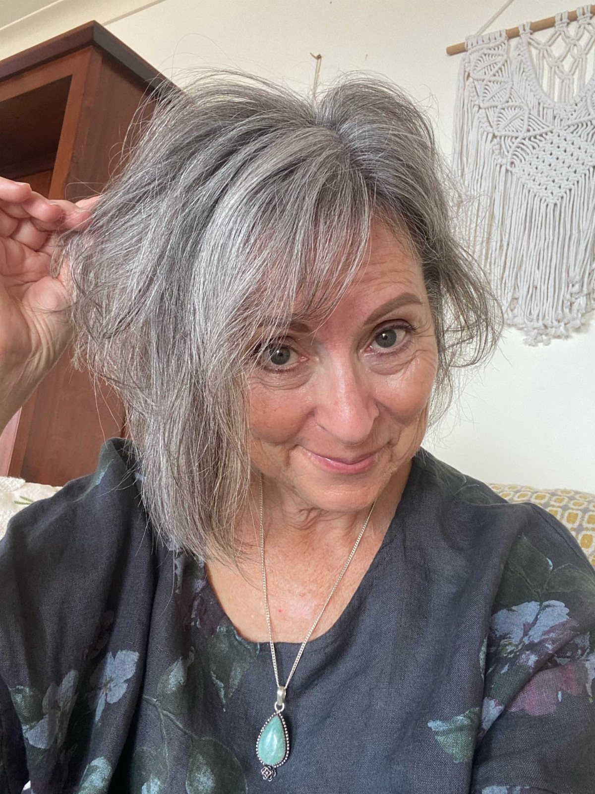 Woman with gray layered shoulder-length hair and bangs lifts a section beside her head