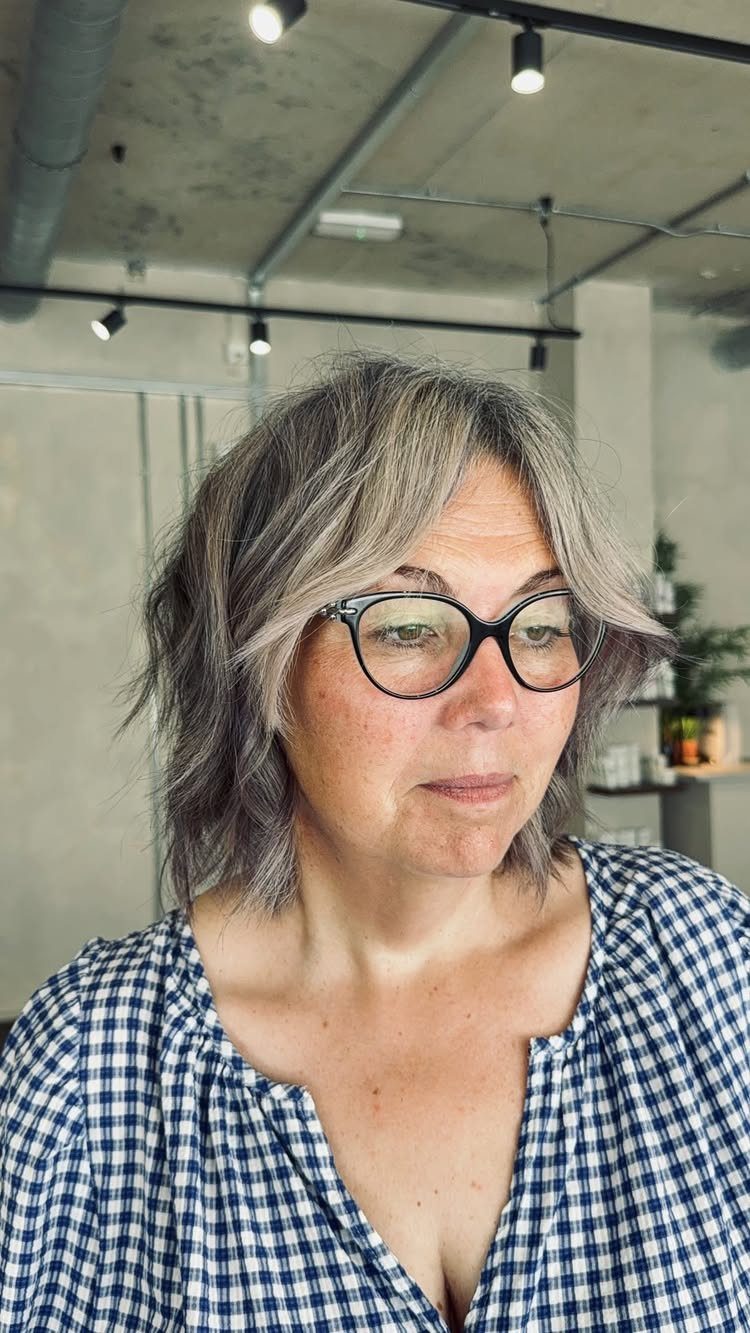 Woman wearing a tousled, choppy gray-brown bob and round glasses