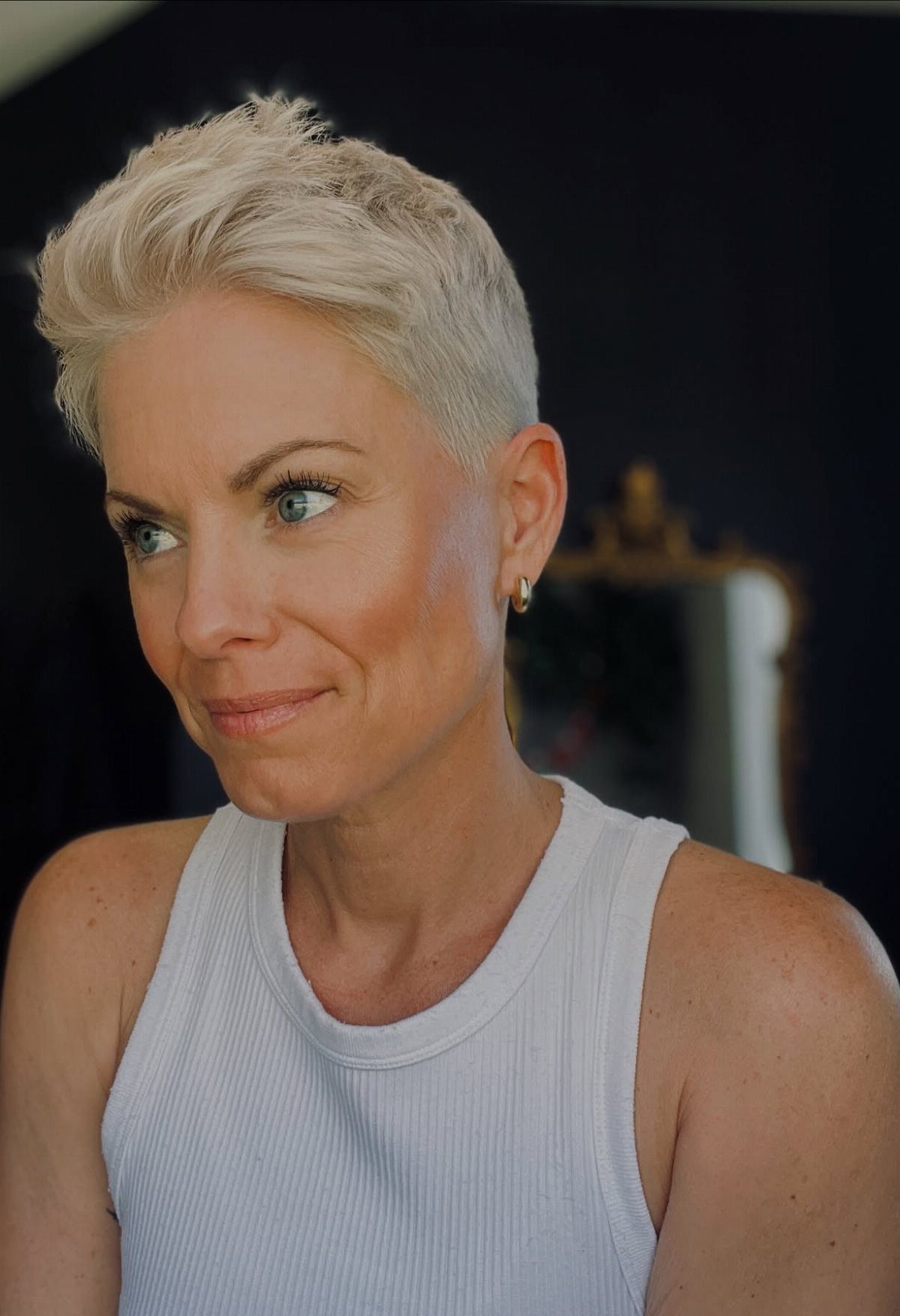 Woman with a short, textured platinum-blonde haircut wearing a white tank top