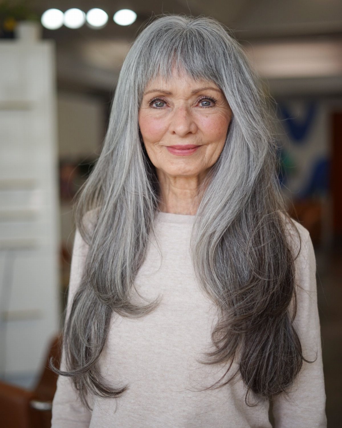 Woman with long silver-gray layers and full bangs posing indoors