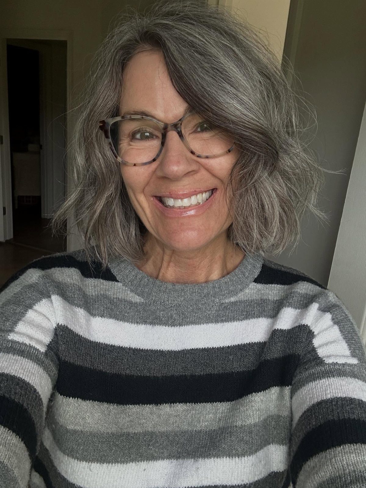 Woman with layered shoulder-length gray hair, glasses, and a striped sweater
