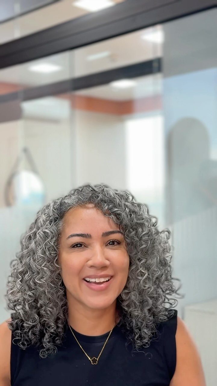 Woman with shoulder-length gray curls smiling indoors near glass windows