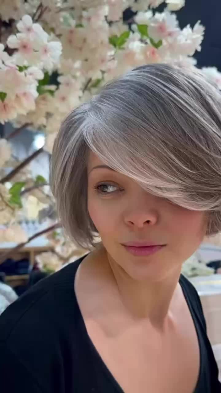 Woman with a blended gray bob and side part posing beneath flowering branches