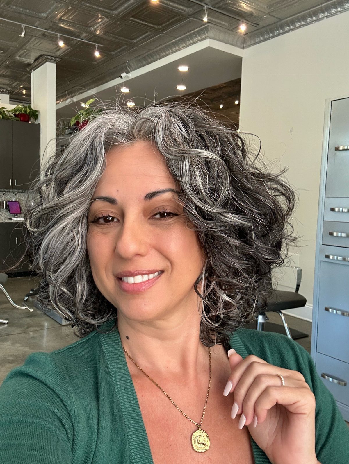 Woman with a deep side-parted salt-and-pepper curly bob in a salon