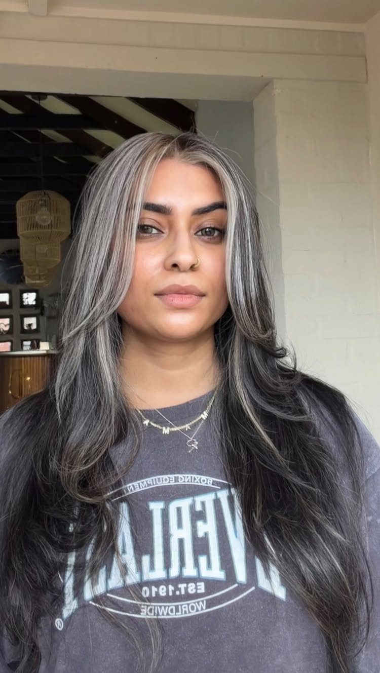 Woman with long dark waves and bright silver highlights framing her face