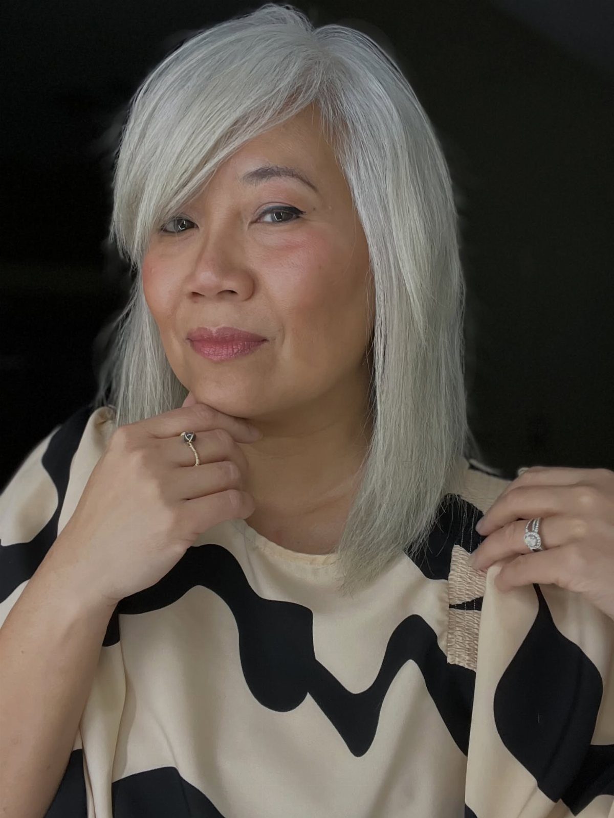 Woman showing her straight, shoulder-length silver-gray hairstyle against a dark background