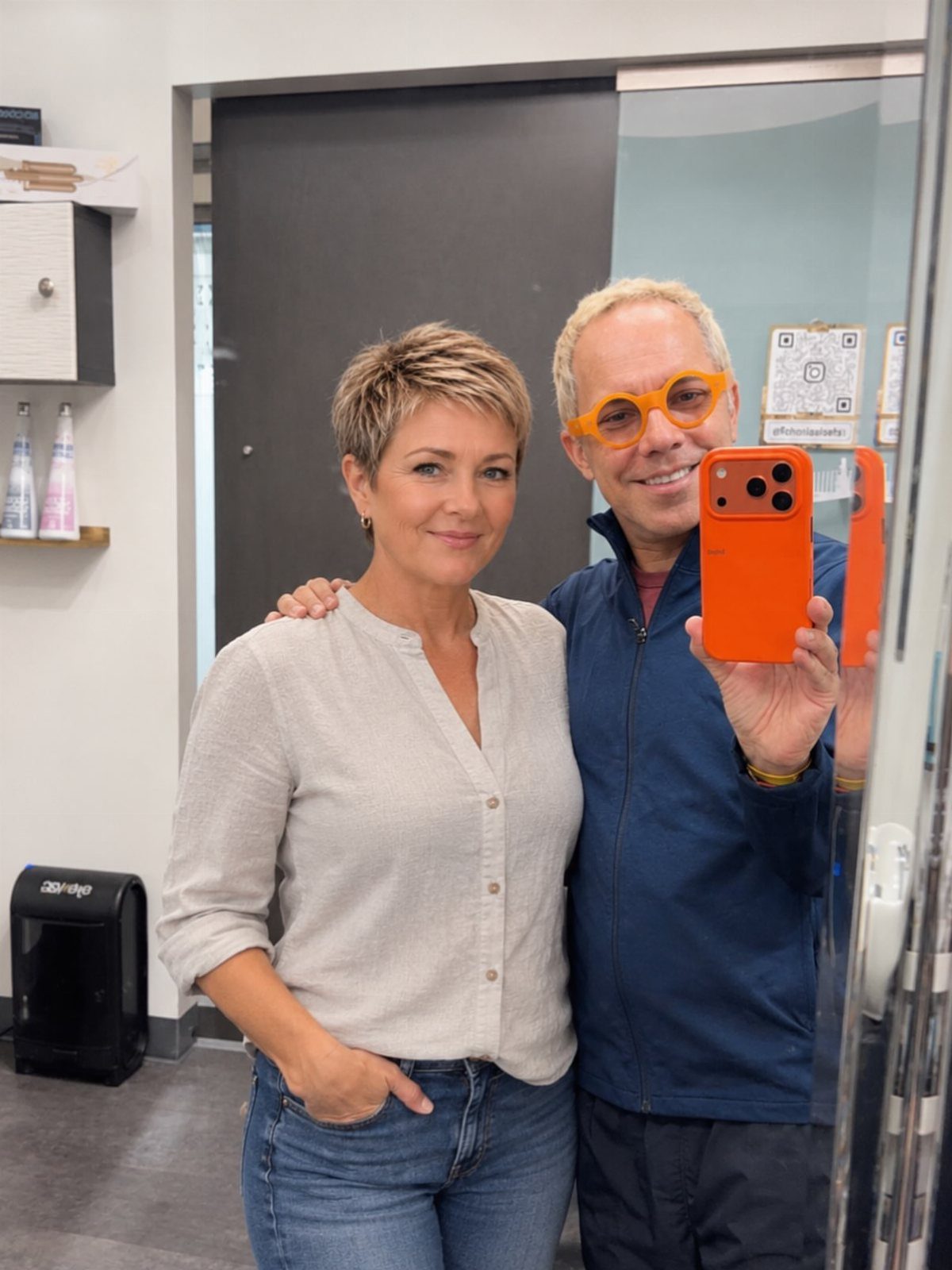 Woman with a short, layered blonde pixie haircut poses in a salon mirror