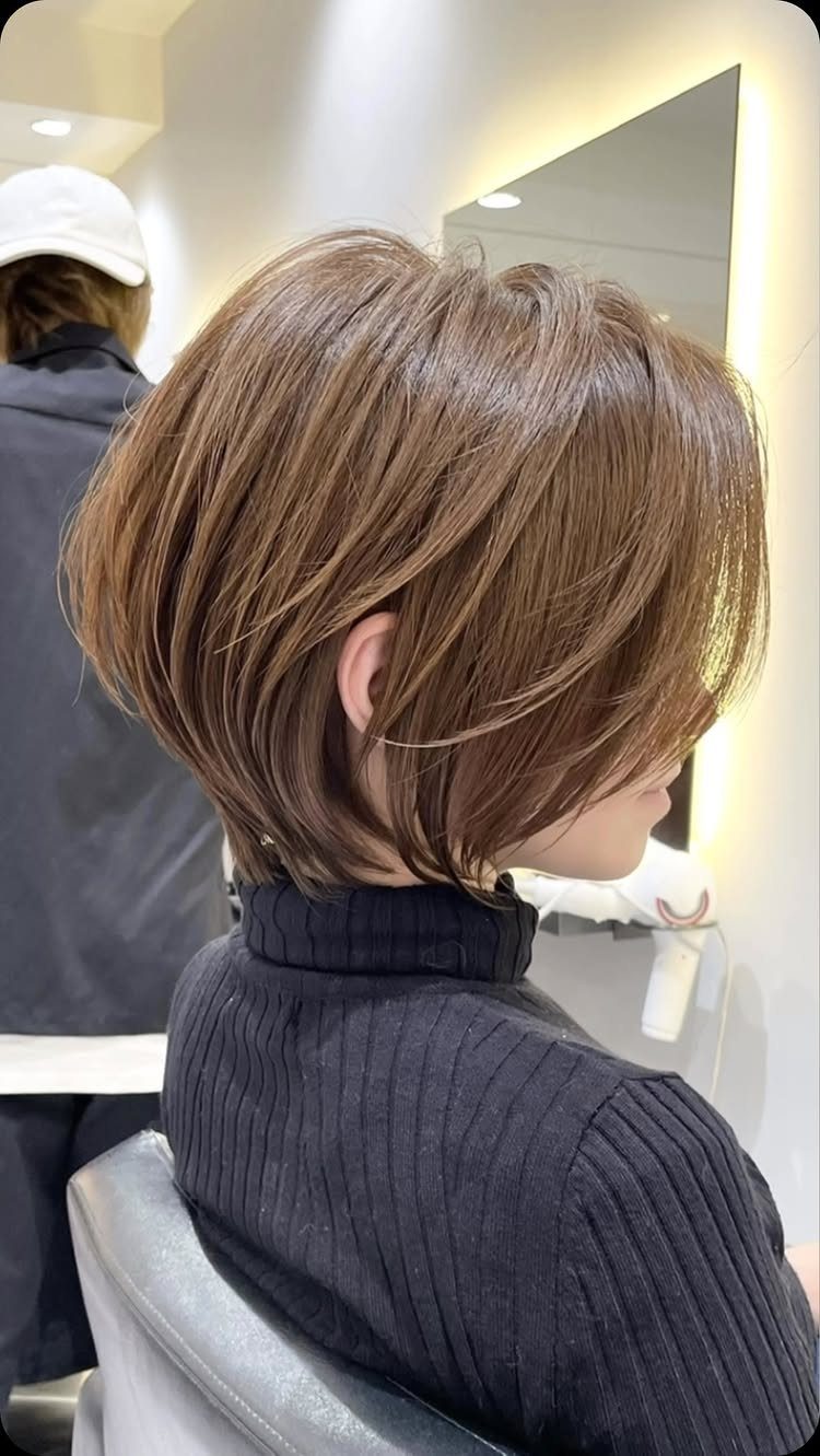 Woman seated in a salon showing a textured, layered brown bob haircut