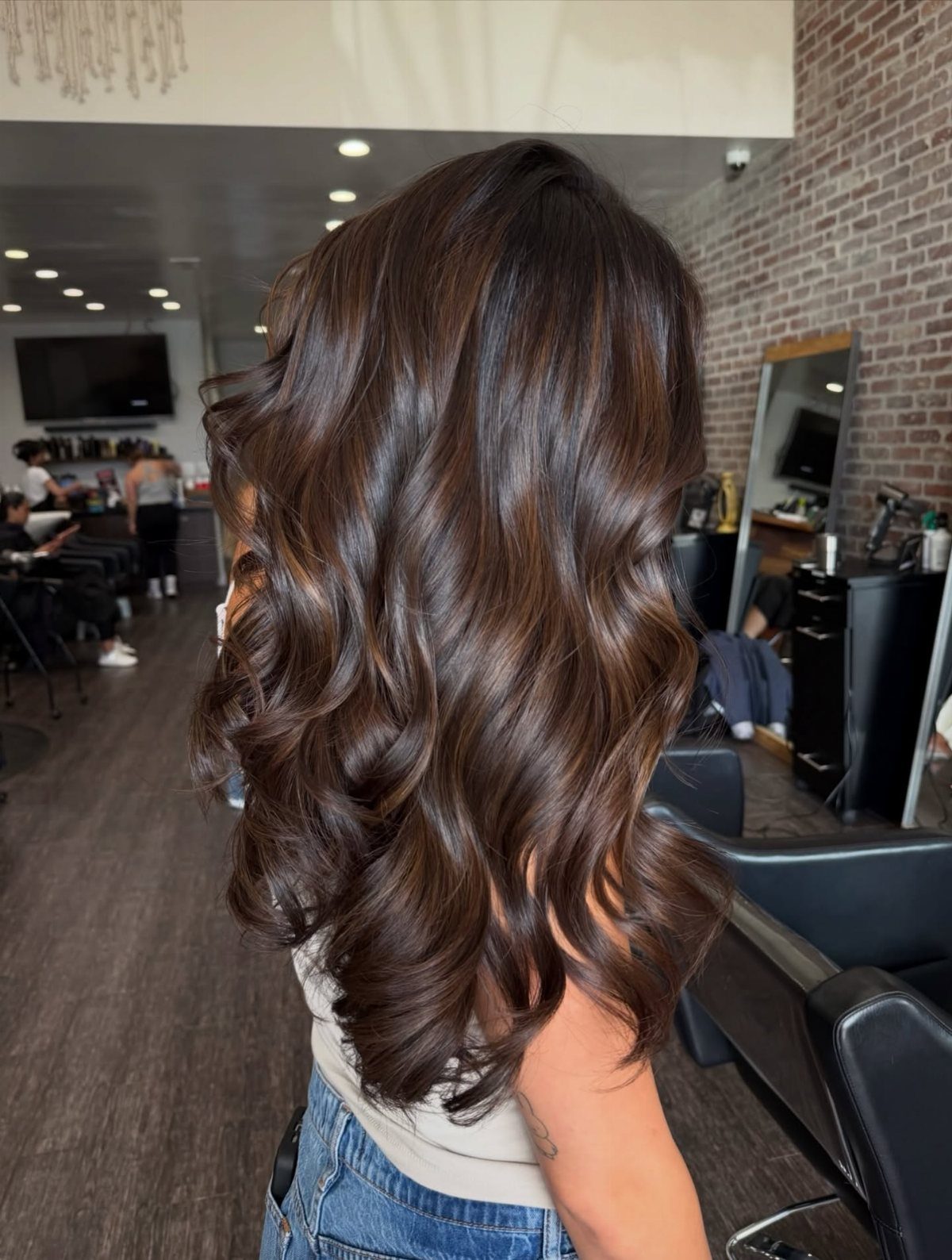 Glossy brunette hair falls in loose, dimensional curls in a salon.