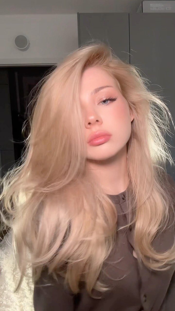 Woman with long, voluminous warm blonde hair posing indoors