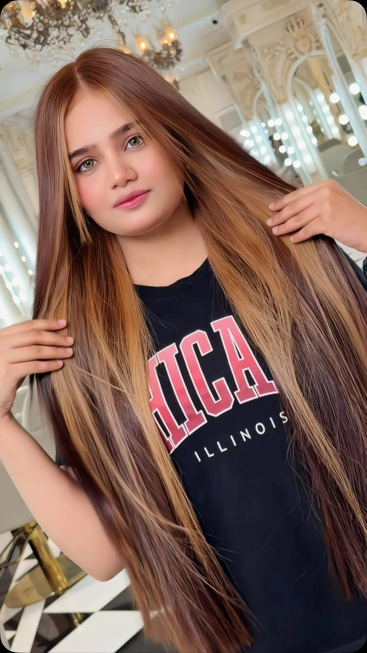 Woman displays long brown hair with caramel-blonde highlights in a salon