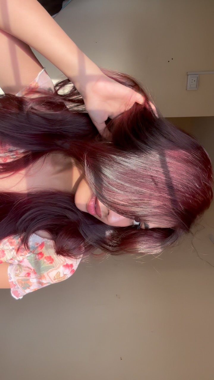 Glossy red-brown hair falls across a person's face as they hold it