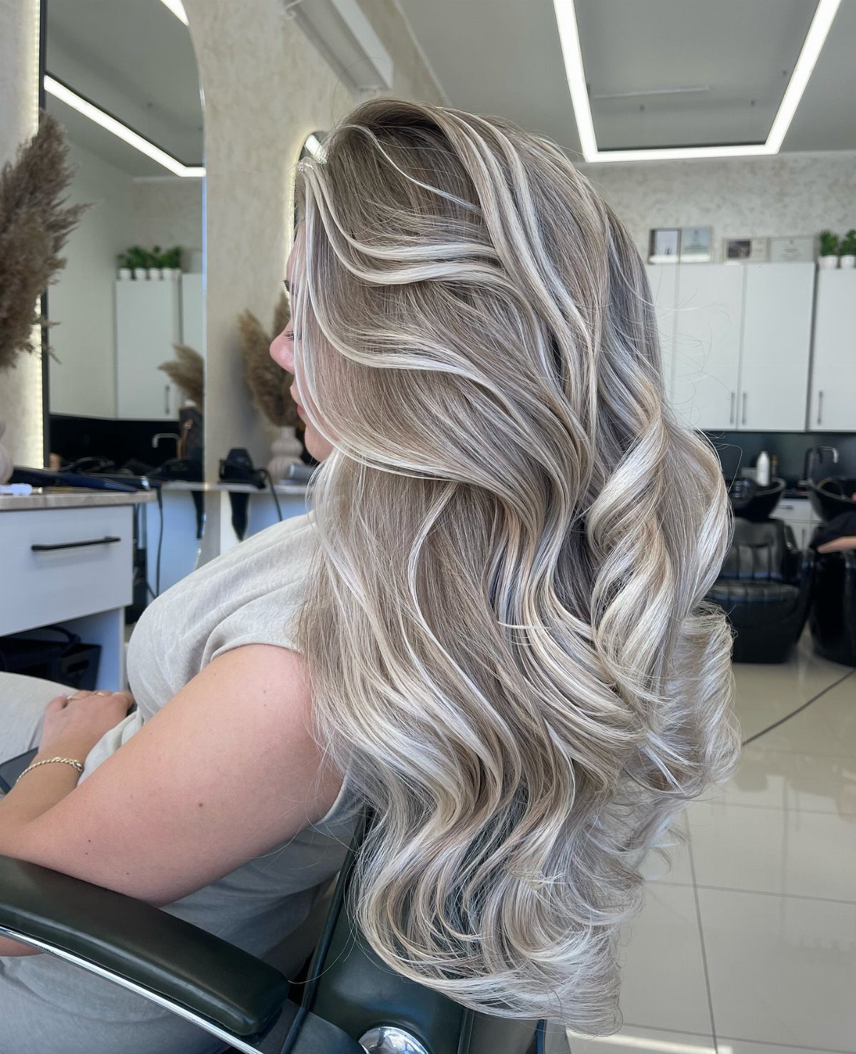 Long ash-blonde curls with cool brunette tones styled in a salon chair.