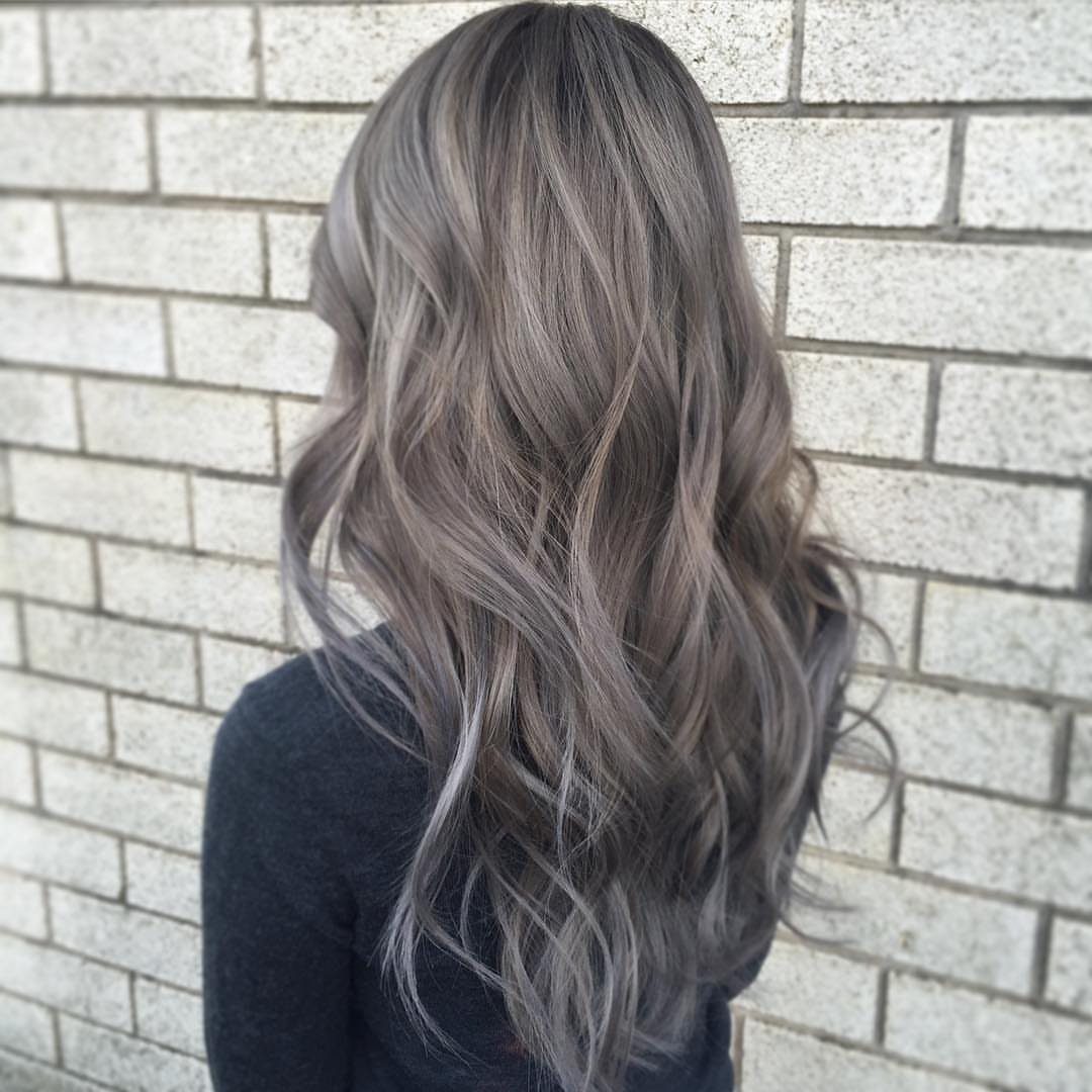Wavy ash-brown hair with blended gray highlights against a white brick wall
