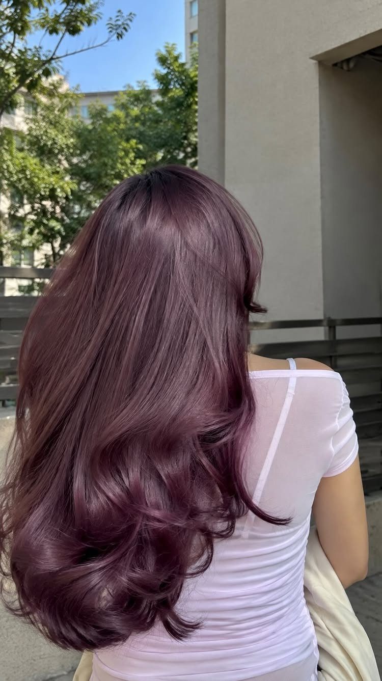 Long plum-purple hair falls in glossy curls over a white shirt outdoors