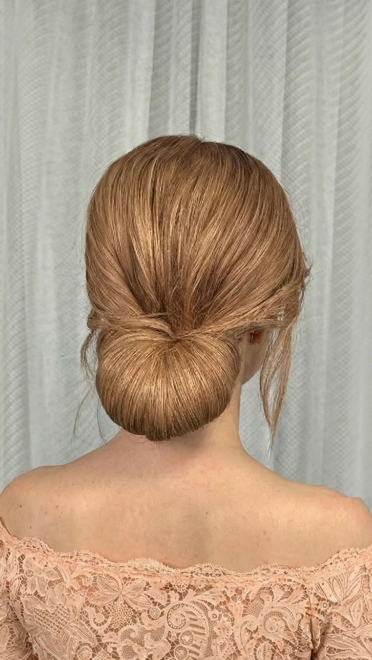Blonde hair styled in a polished low chignon above a pale pink lace top