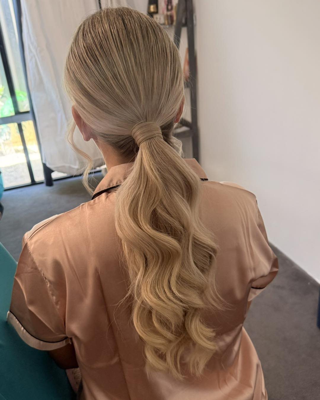 Long blonde hair styled in a low ponytail with cascading curls
