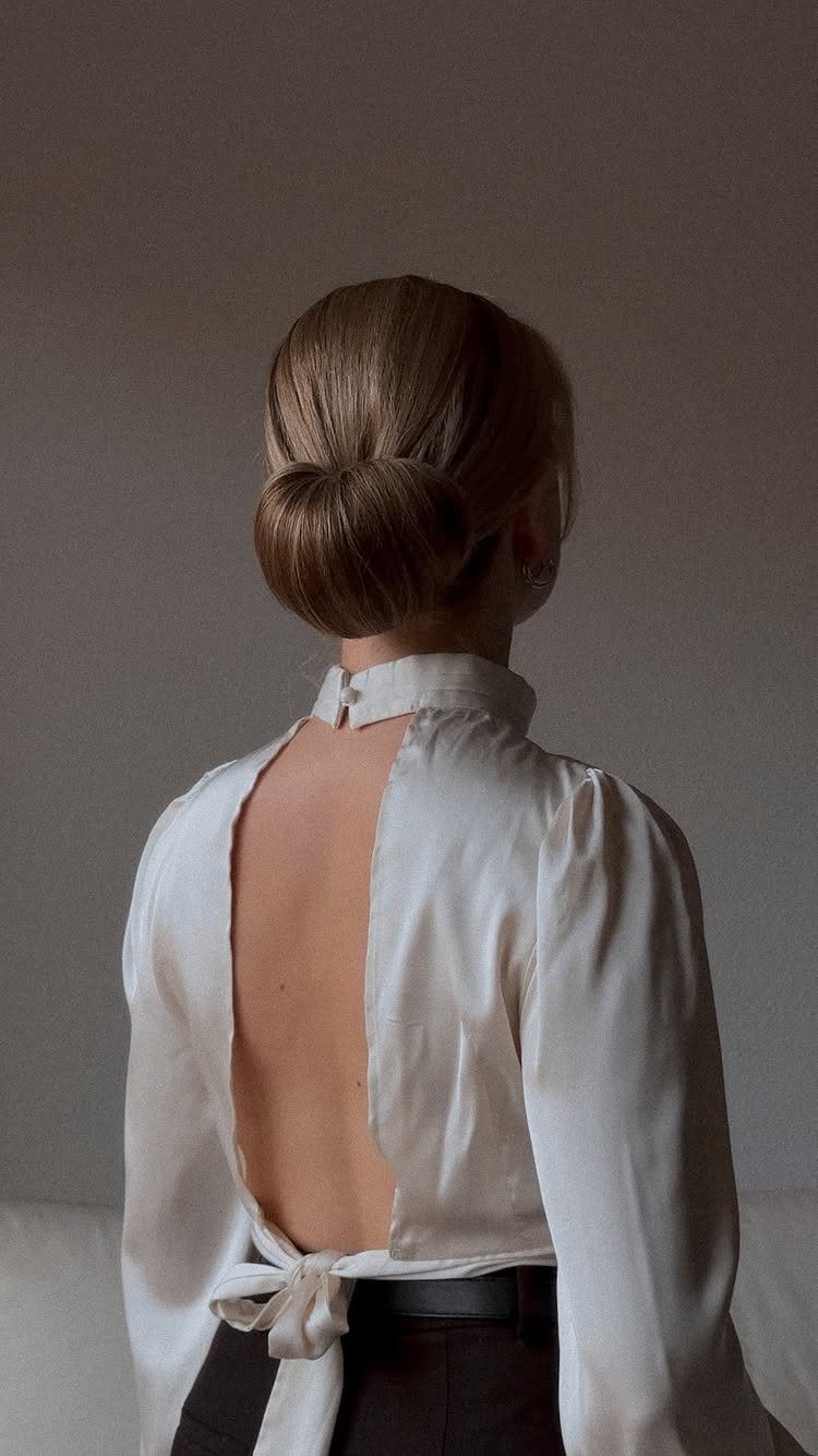 Smooth brown hair gathered into a neat low bun above a white satin blouse