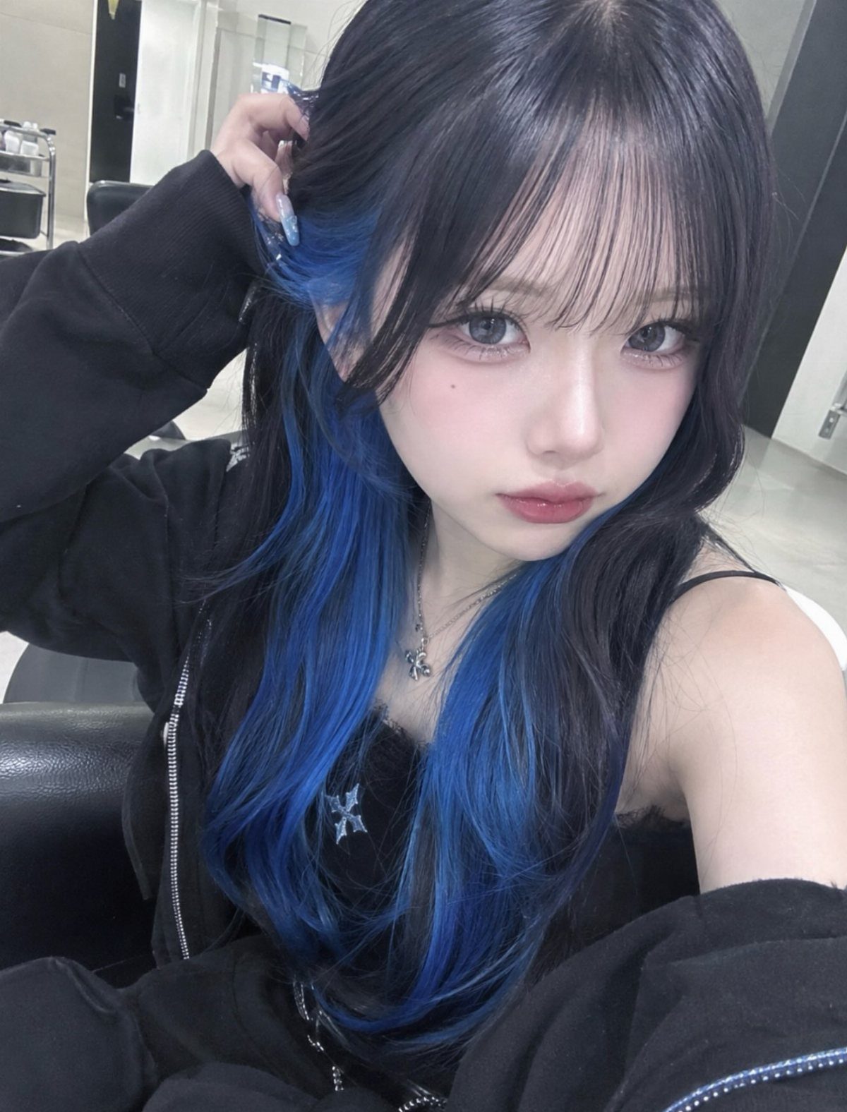 Woman with long black hair and vivid cobalt-blue underlayers posing indoors.