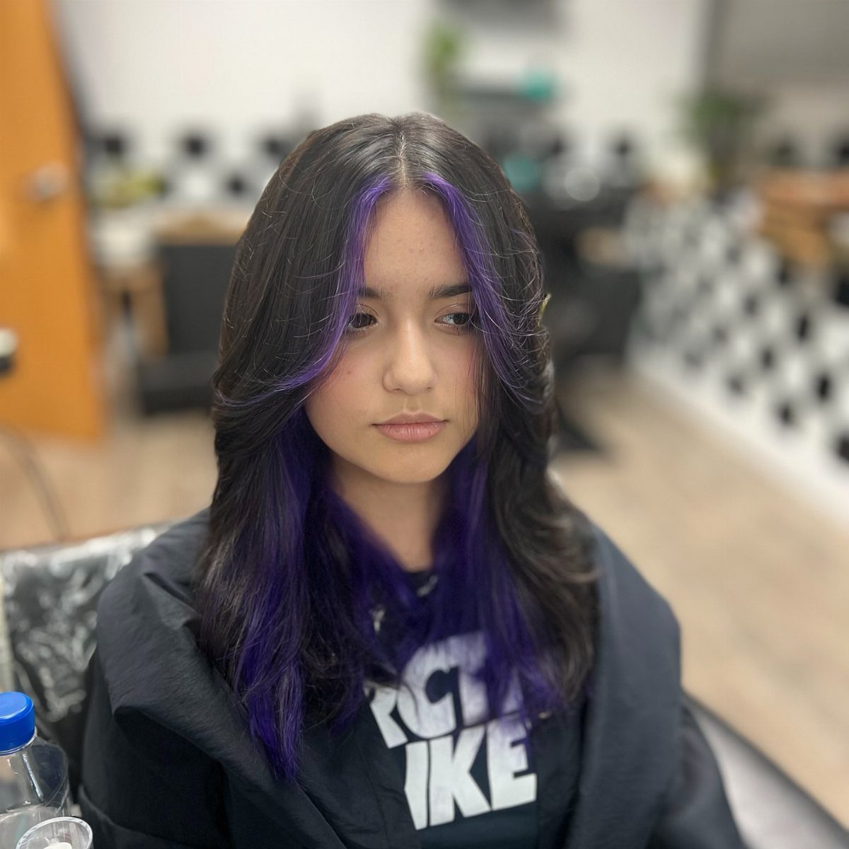 Long black hair with violet-purple face-framing and underneath sections in a salon