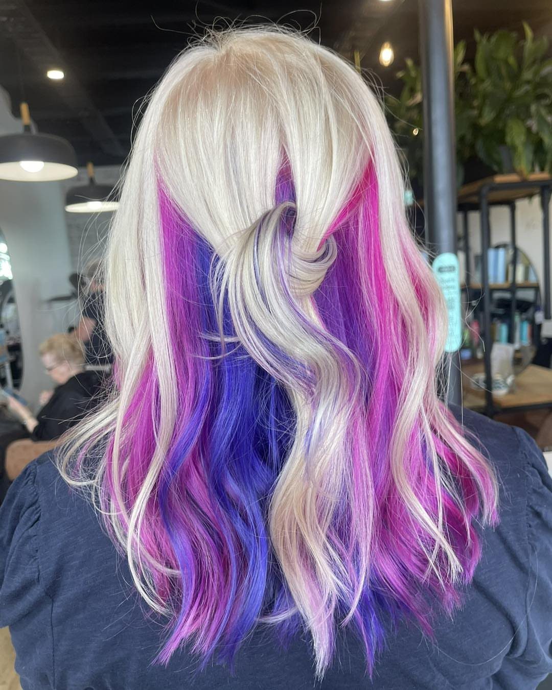 Platinum-blonde waves reveal vivid pink and purple peekaboo underlayers in a salon