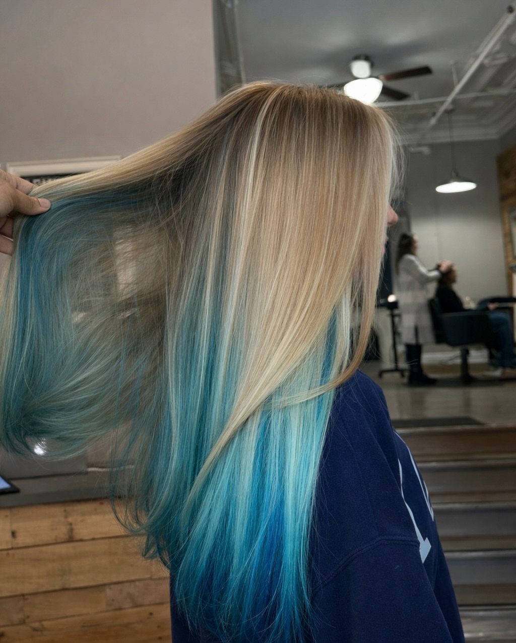Blonde hair lifted to reveal vivid turquoise-blue peekaboo underlayers in a salon