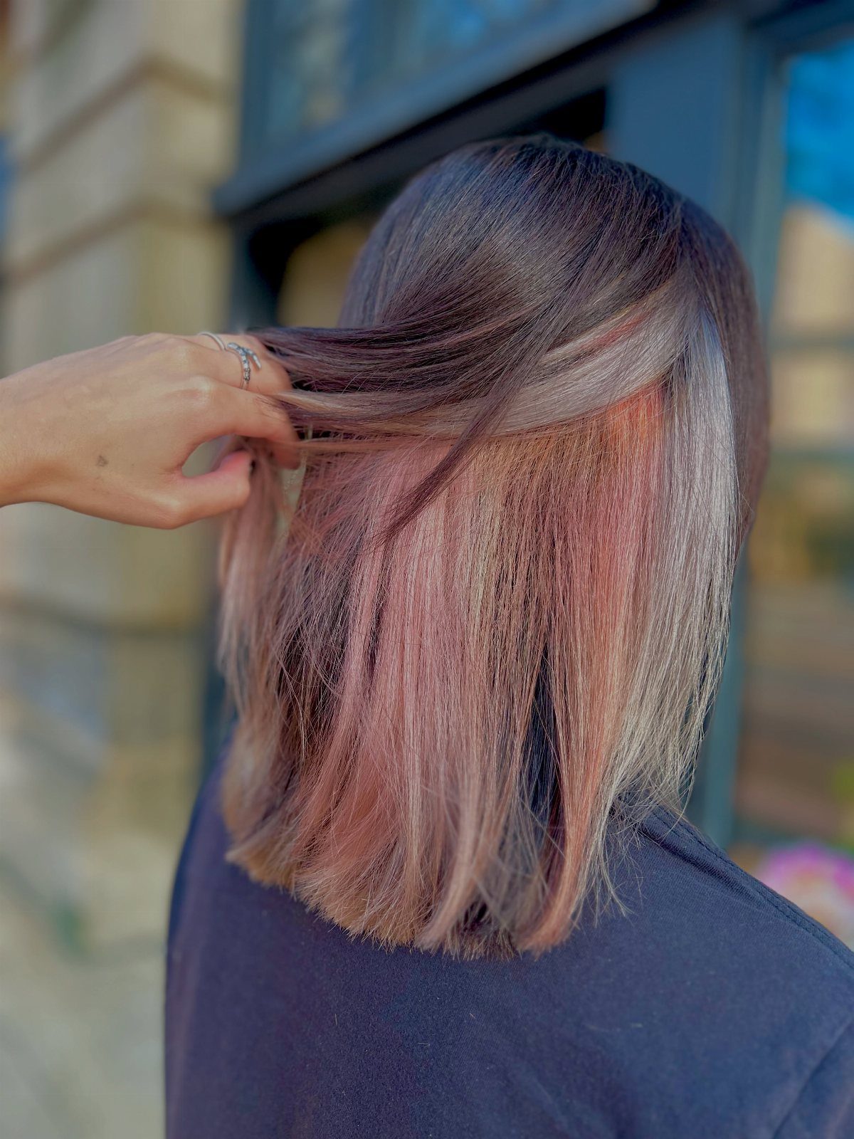 Dark brown hair reveals rose-gold and pale pink underlayers as a hand lifts it
