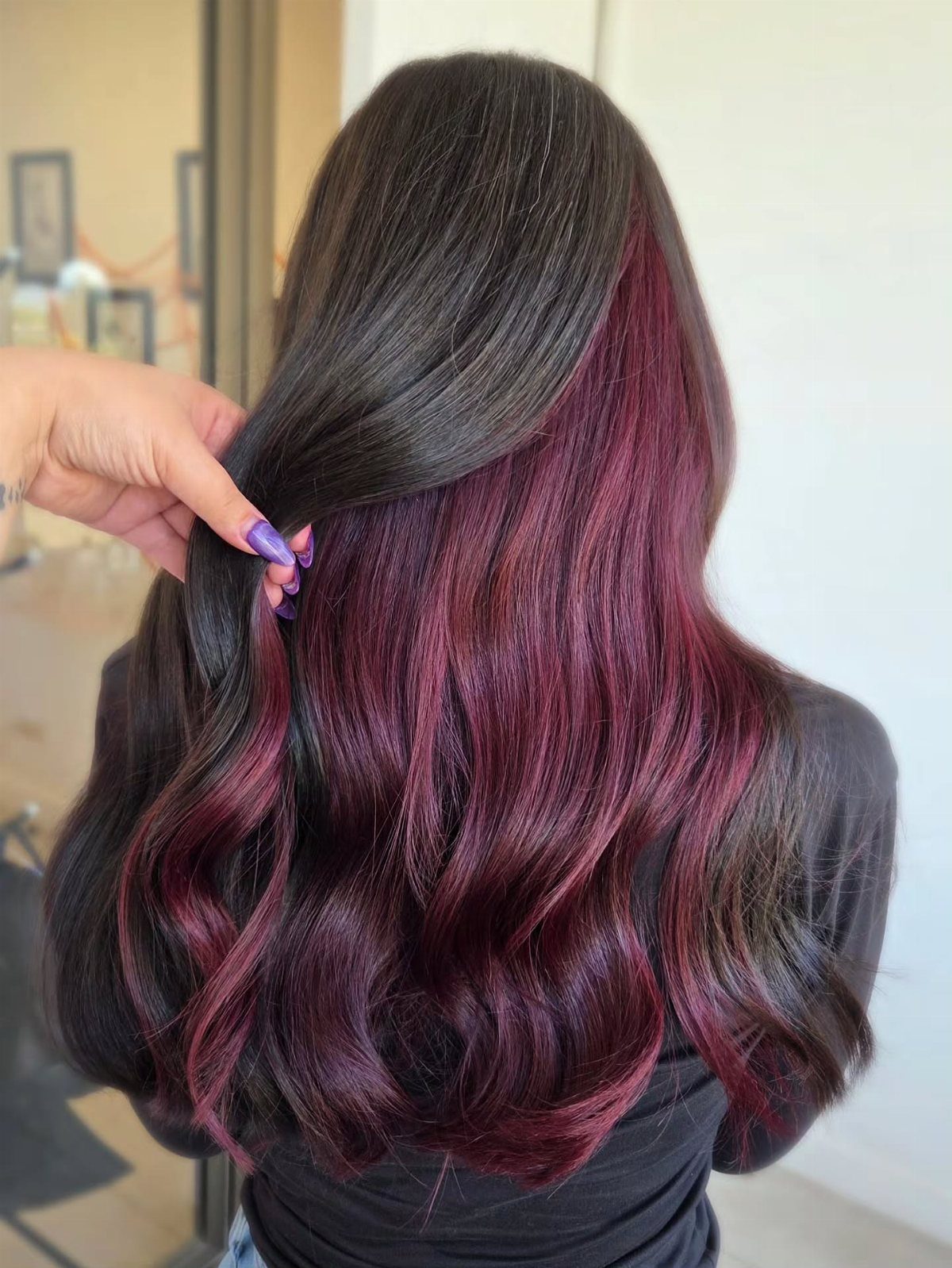 Dark wavy hair reveals deep burgundy peekaboo sections underneath