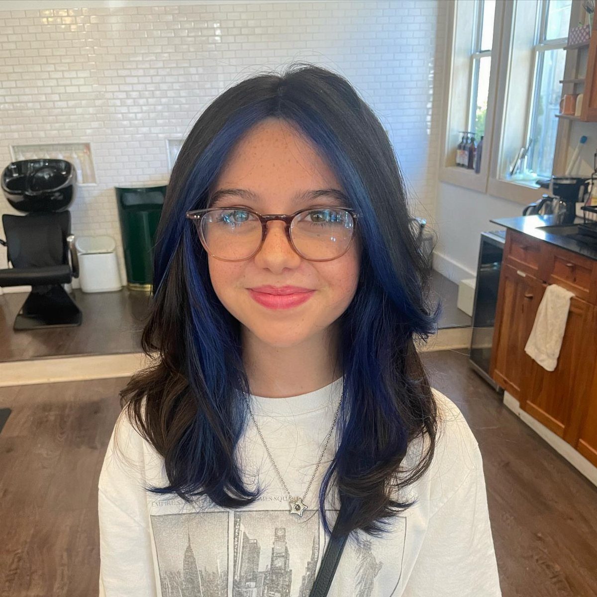 Dark-haired person with vivid blue face-framing sections in a salon