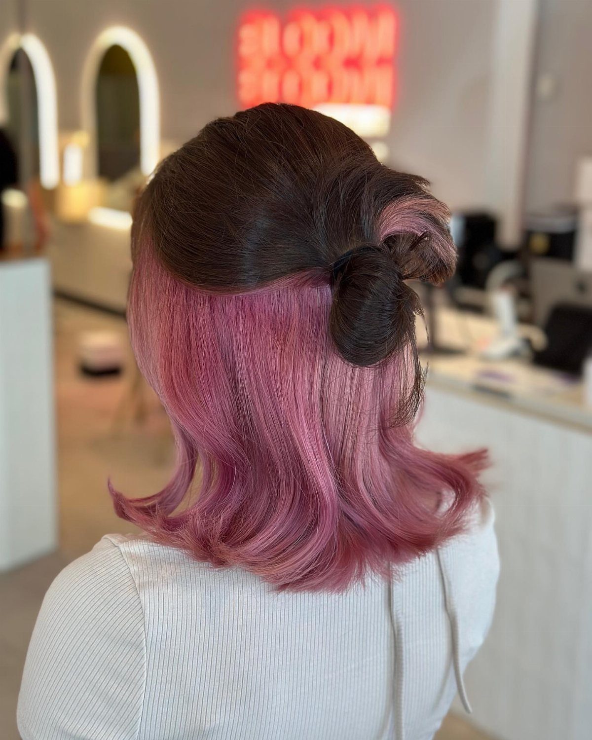 Dark-haired person reveals pink peekaboo underlayers in a salon
