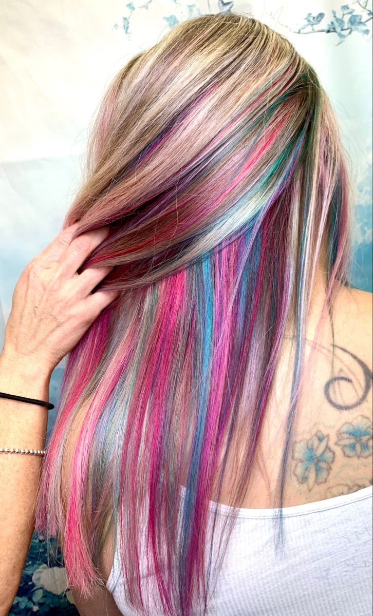 Long layered hair reveals bright pink and teal streaks beneath blonde-brown top layers