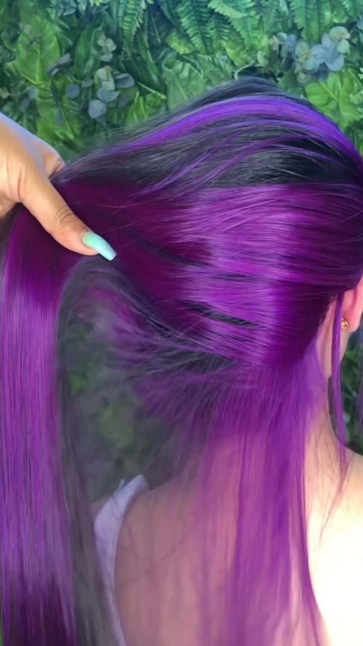 Dark hair lifted to reveal vivid purple-magenta underlayers against green foliage