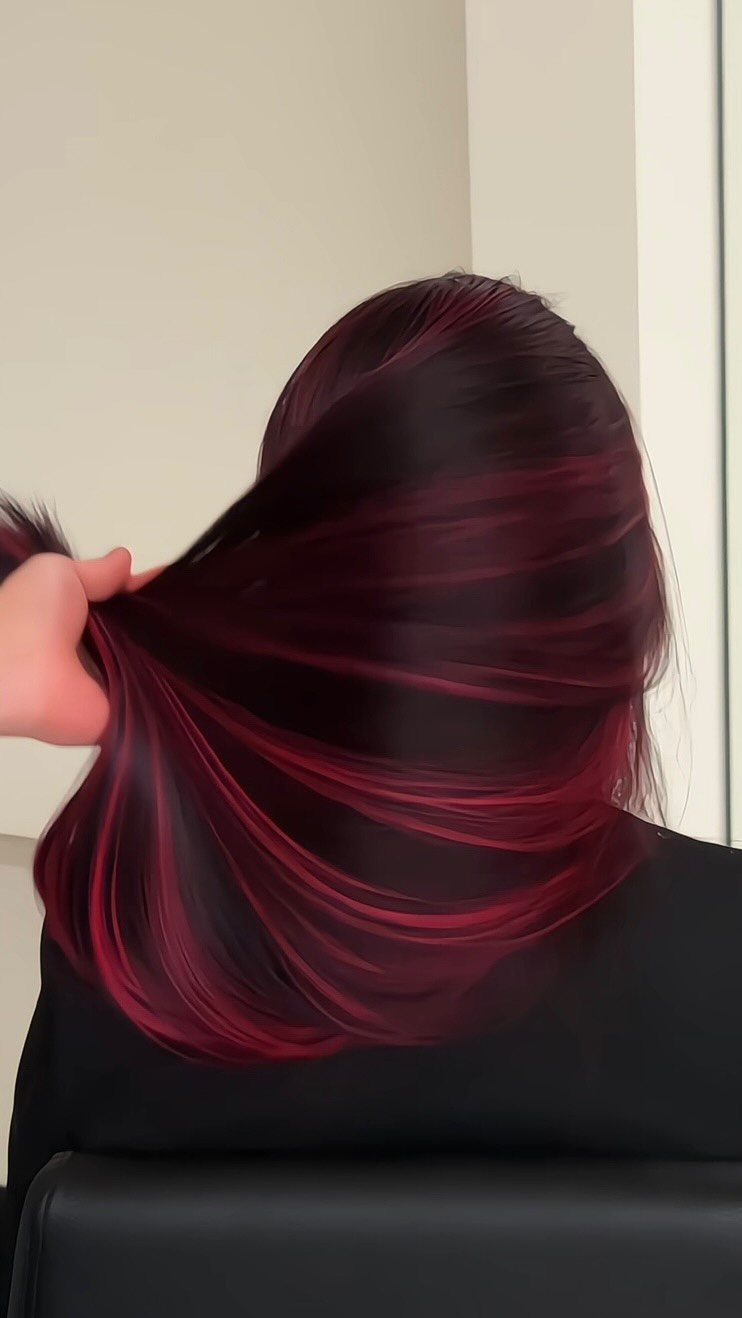 Dark hair lifted by a hand reveals vivid red peekaboo sections underneath.