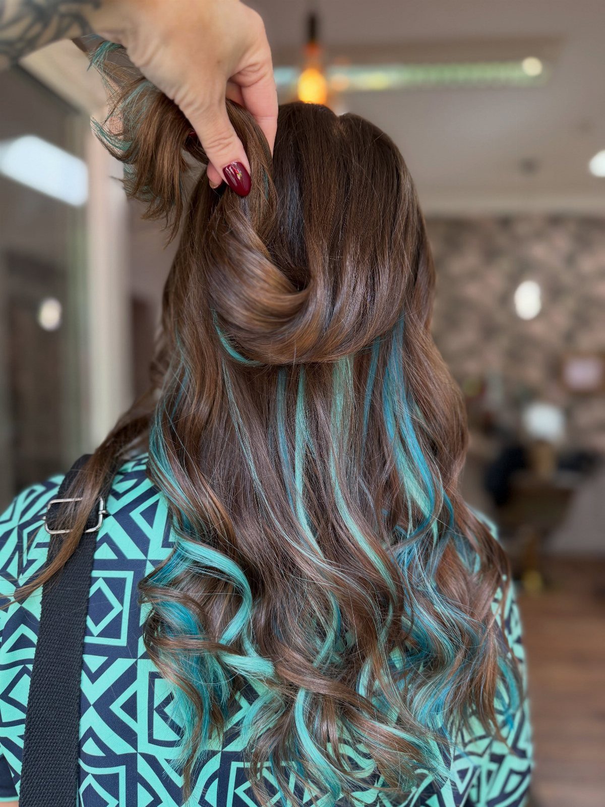 Wavy brown hair lifted to reveal vivid teal peekaboo underlayers