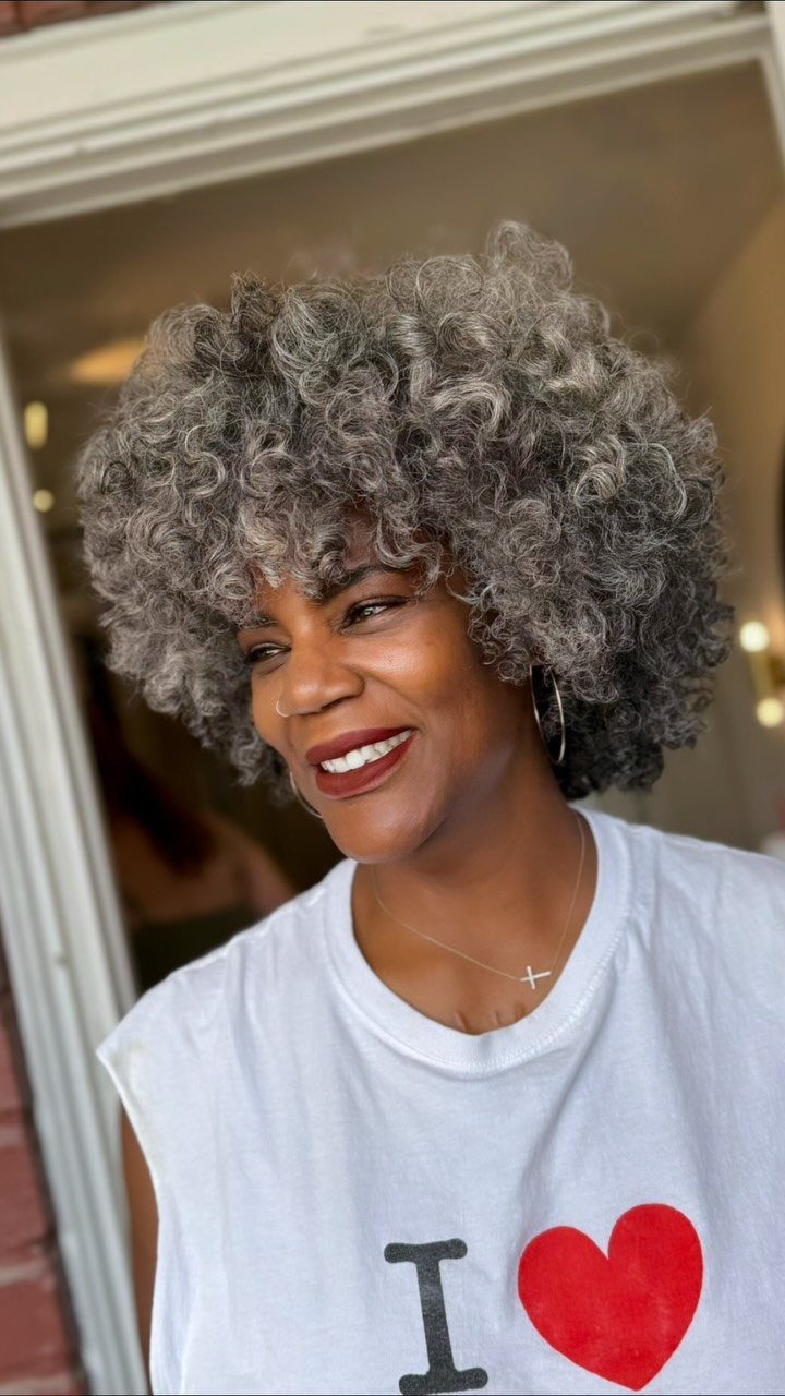 Woman smiling with dense salt-and-pepper curls framing her face