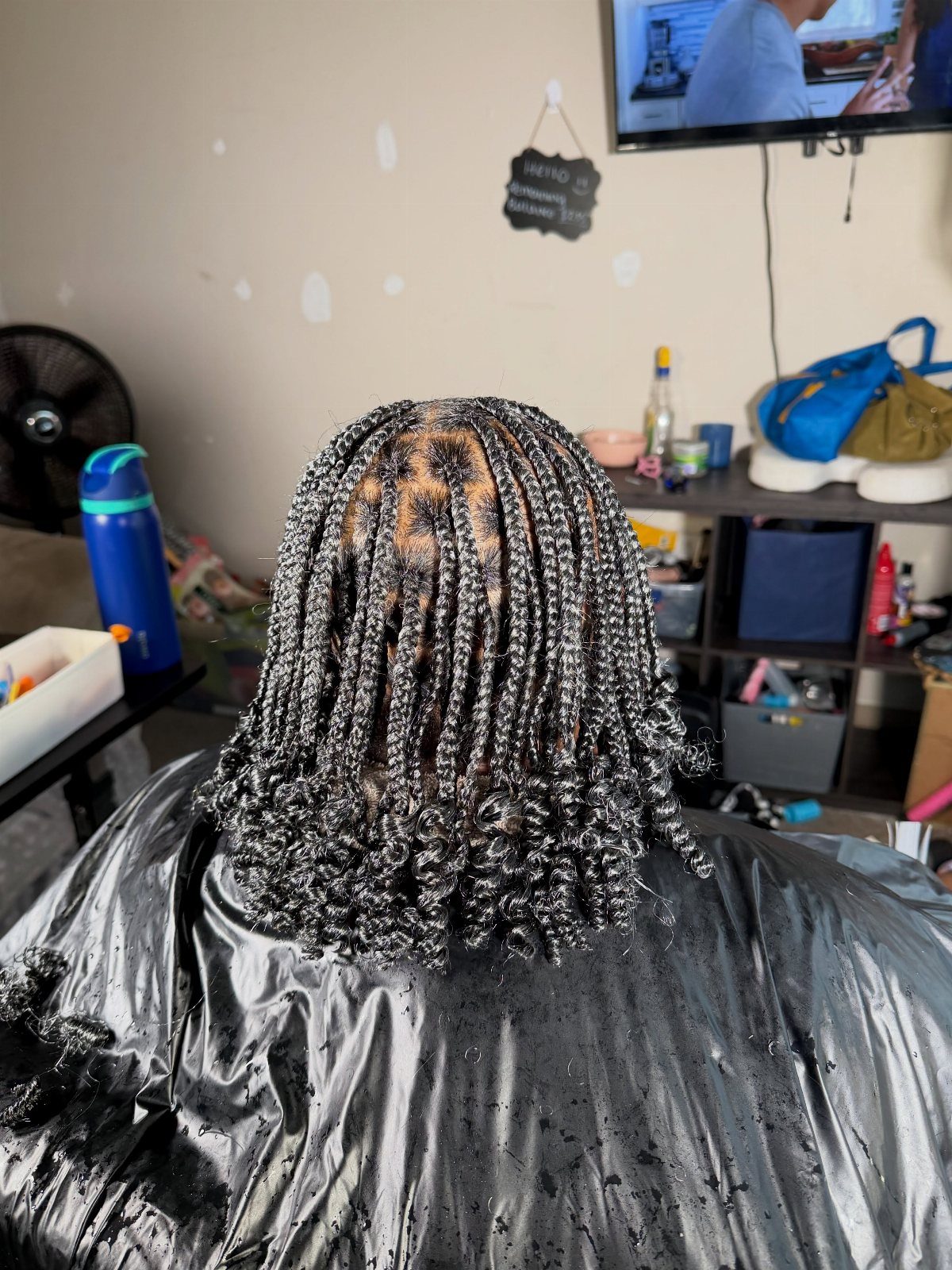 Long black and silver-gray braids hang over a salon cape