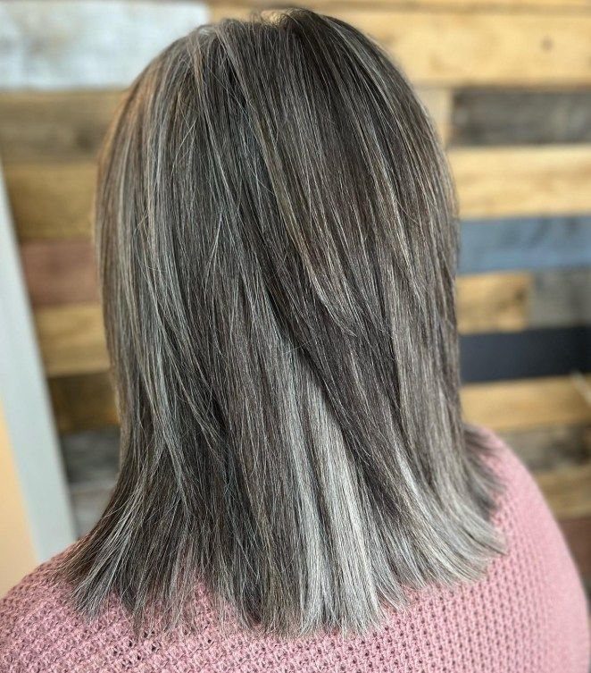 Shoulder-length straight salt-and-pepper hair falls over a pink knit top.