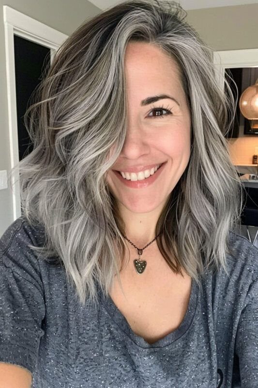 Woman with shoulder-length salt-and-pepper waves smiles indoors