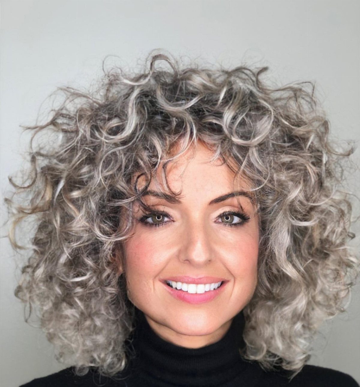 Woman with a voluminous curly silver-beige bob and a black high-neck top