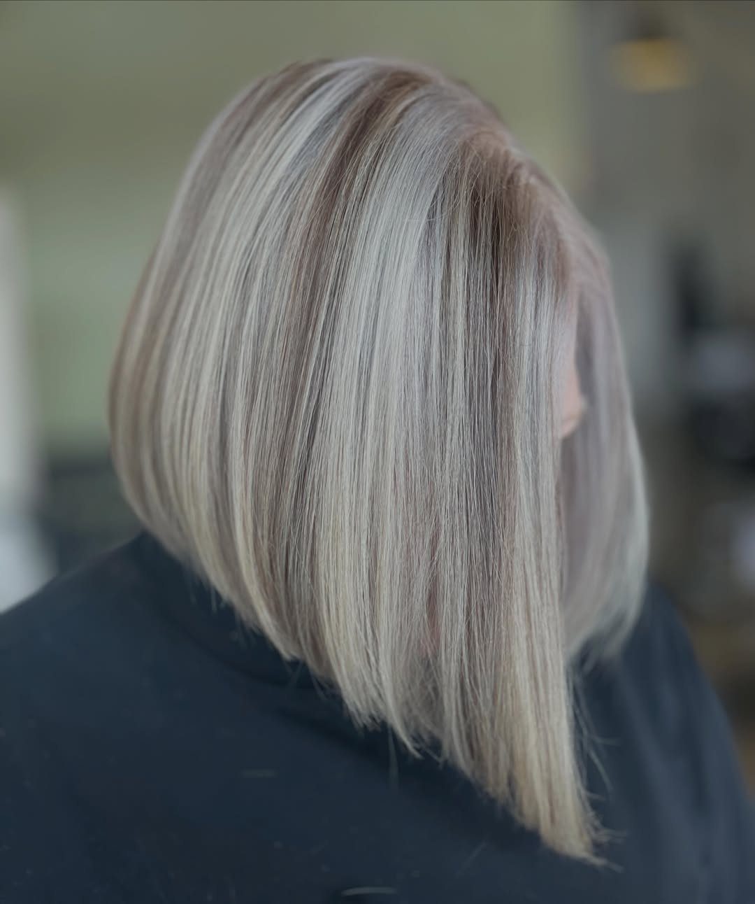 Silver-gray bob with longer front sections and darker roots, shown in a salon