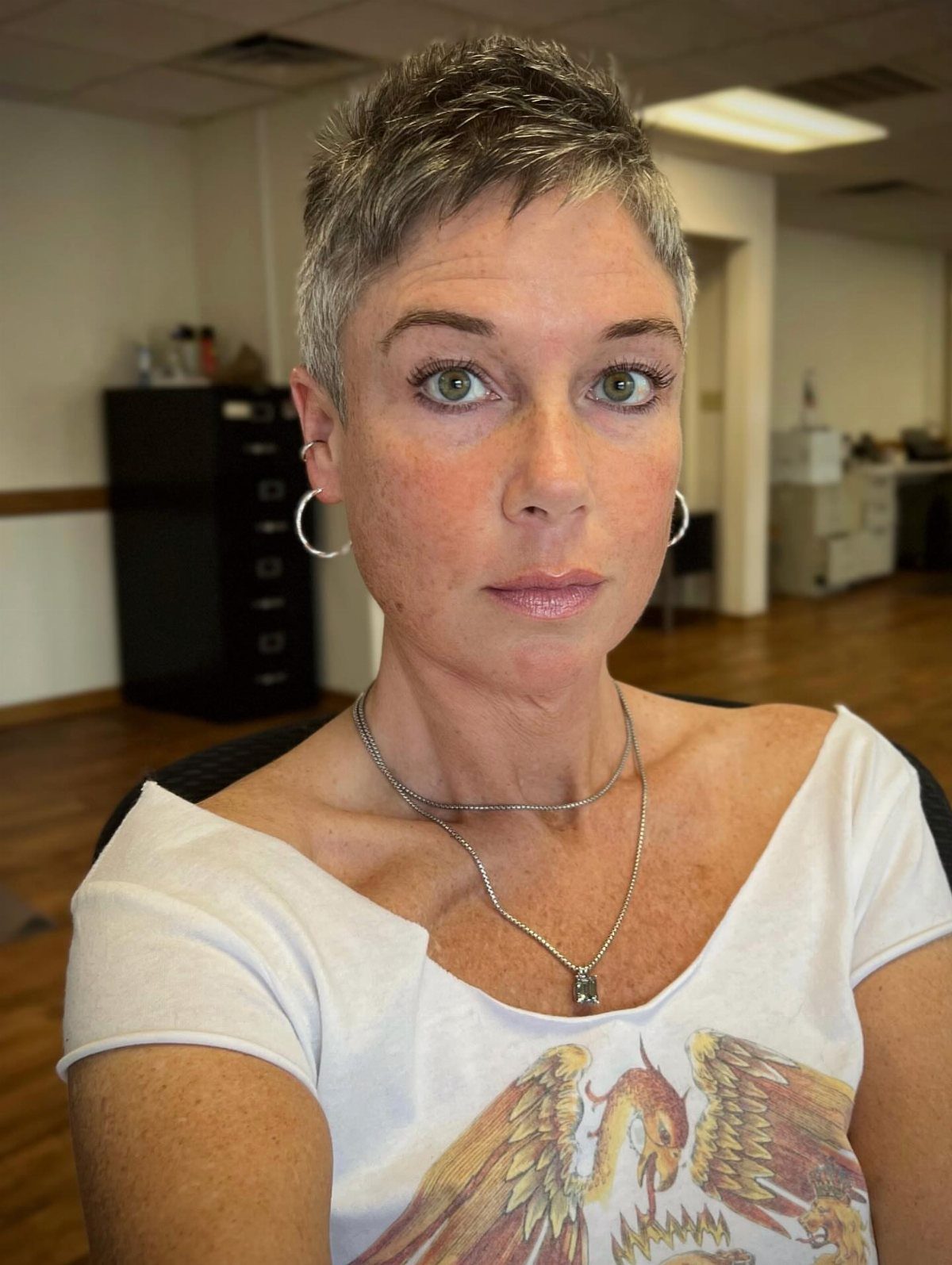 Woman with a short, textured gray-brown pixie haircut and a white graphic T-shirt