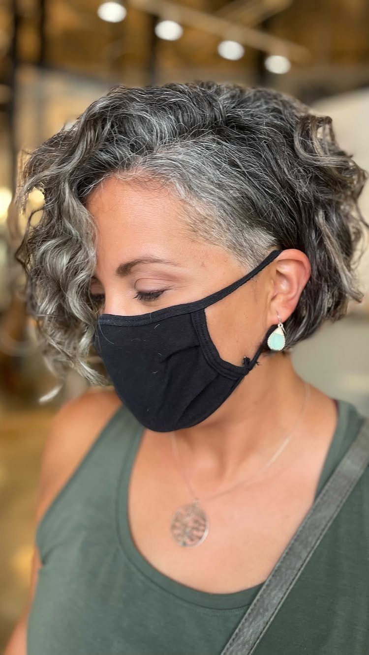 Woman with short wavy gray hair wearing a black mask and green top