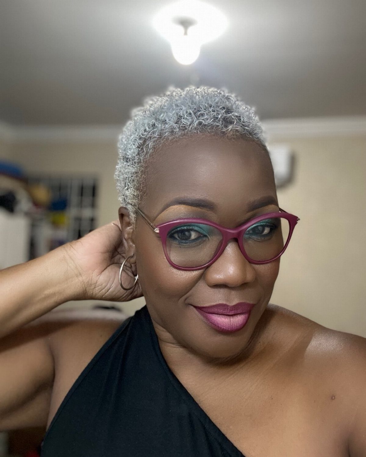 Woman wears short, rounded silver-gray coils with magenta glasses