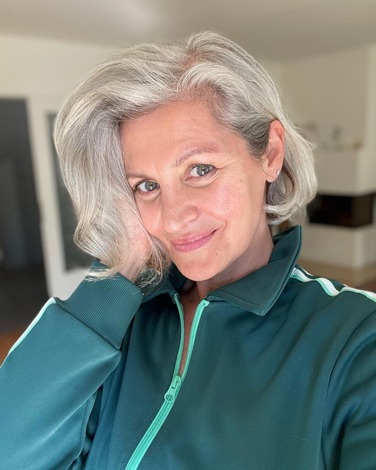 Woman with a wavy silver-gray bob wearing a teal zip-up top