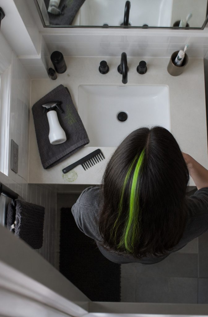 Neon green temporary color on a hair streak beside its spray product