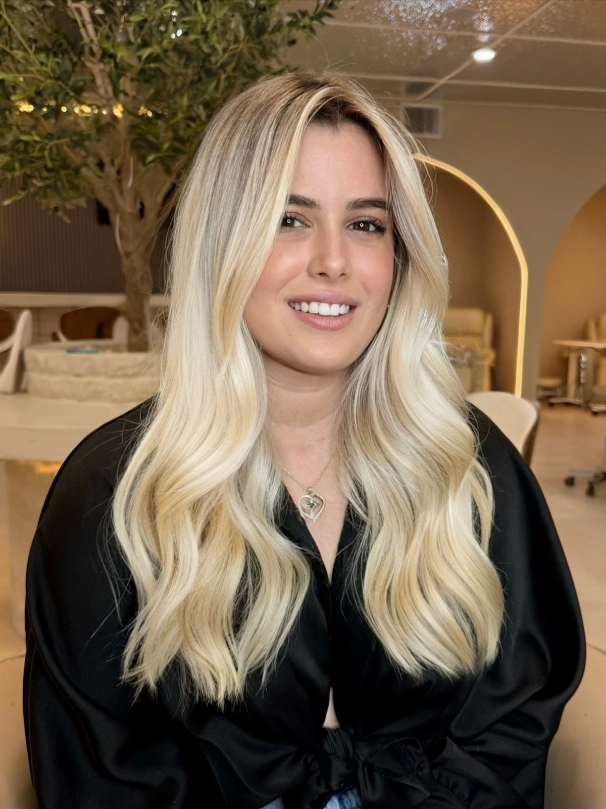 Woman with long, wavy creamy blonde hair and darker roots in a black blouse