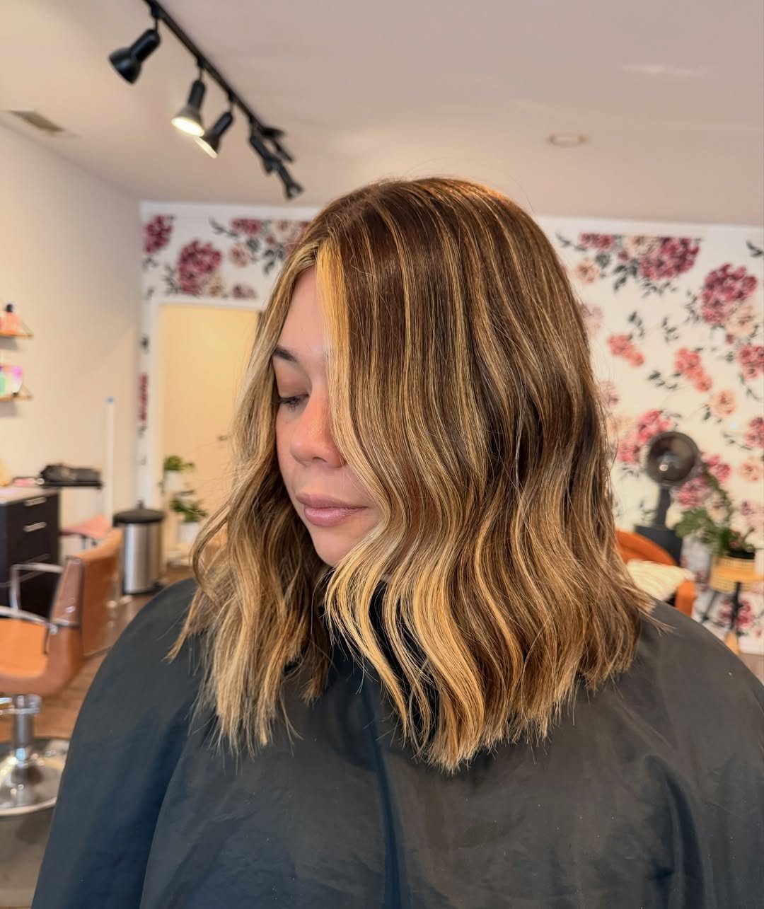 Woman with shoulder-length wavy brown hair and warm caramel highlights in a salon