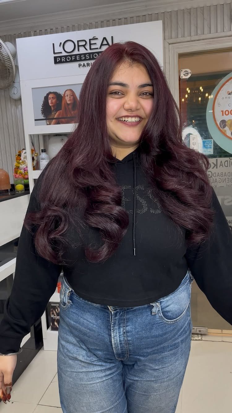Woman with long, glossy cherry-burgundy hair in loose curls at a salon