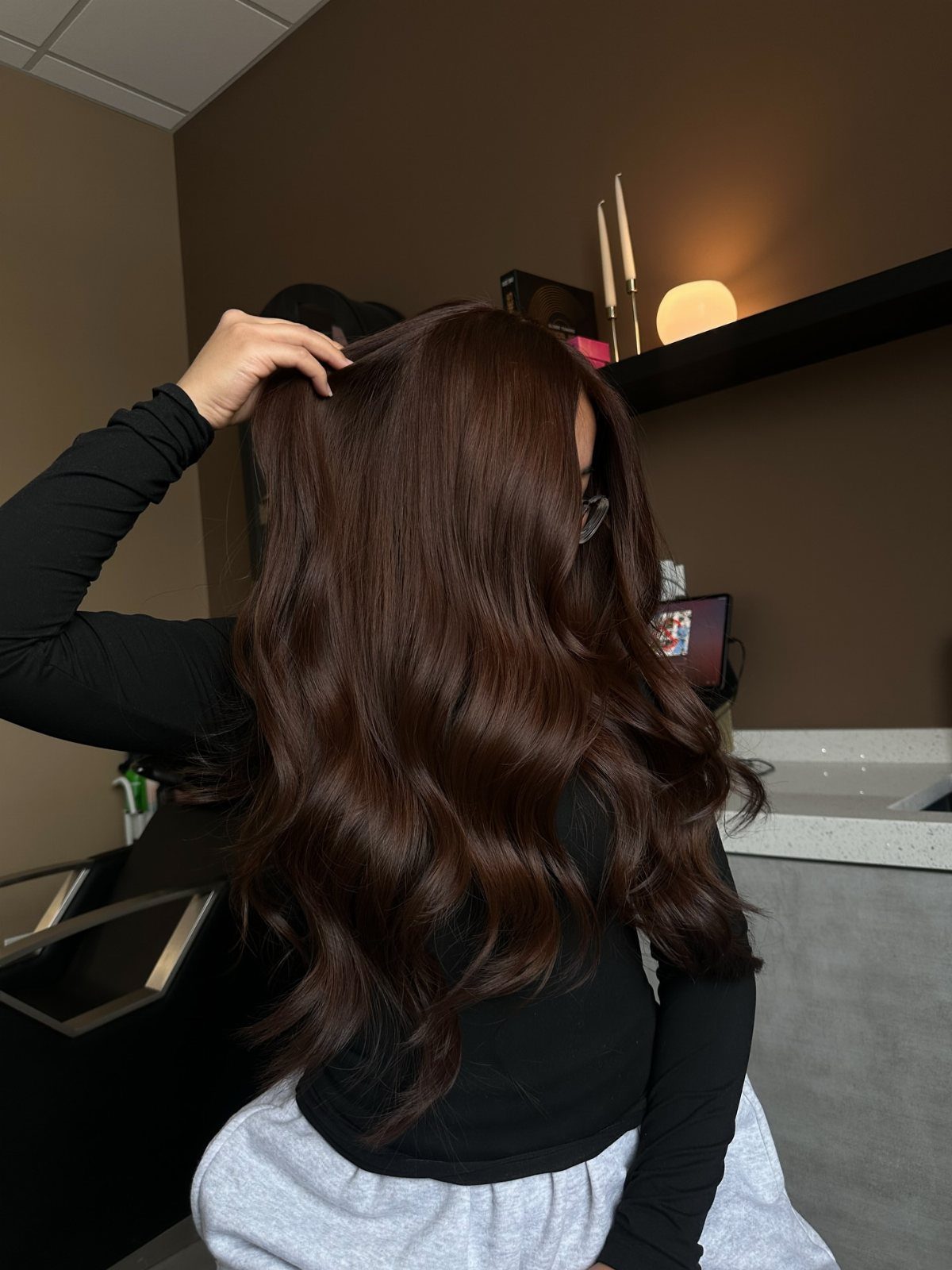 Glossy chocolate-brown hair falls in long, softly curled waves in a salon.