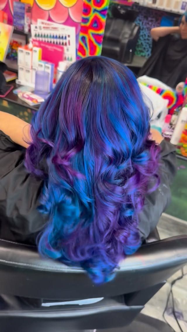 Blue and purple jewel-toned curls cascade down a salon client's back